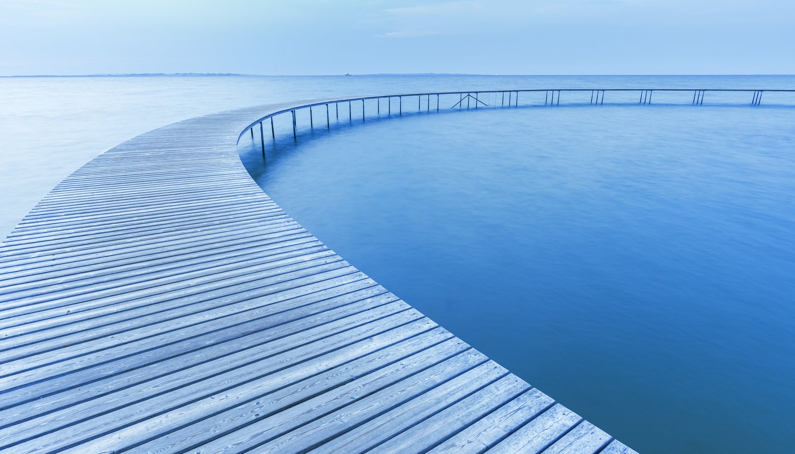 A curved boardwalk crossing calm water, representing a careful migration to a new platform