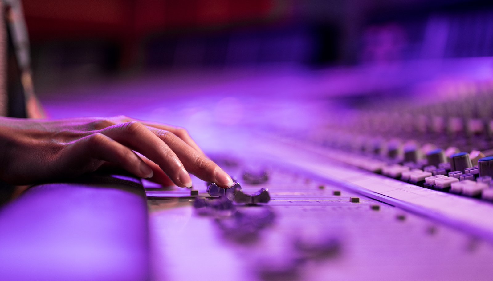 A hand adjusting faders on a studio mixing console, representing a person operating a complex system with help from an assistant